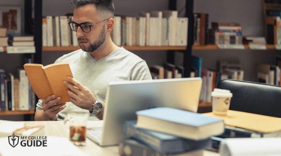Man taking Online History Degree researching in library